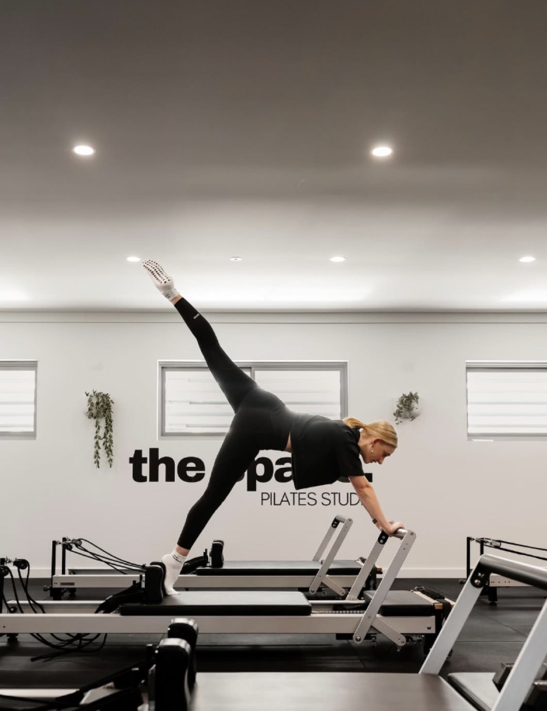 A member holding a standing side-star position on the reformer, in front of The Space signage