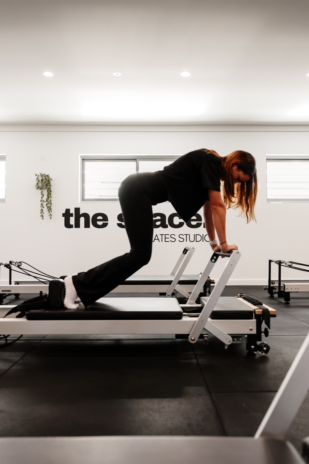 An instructor climbing onto a reformer in front of The Space wall logo