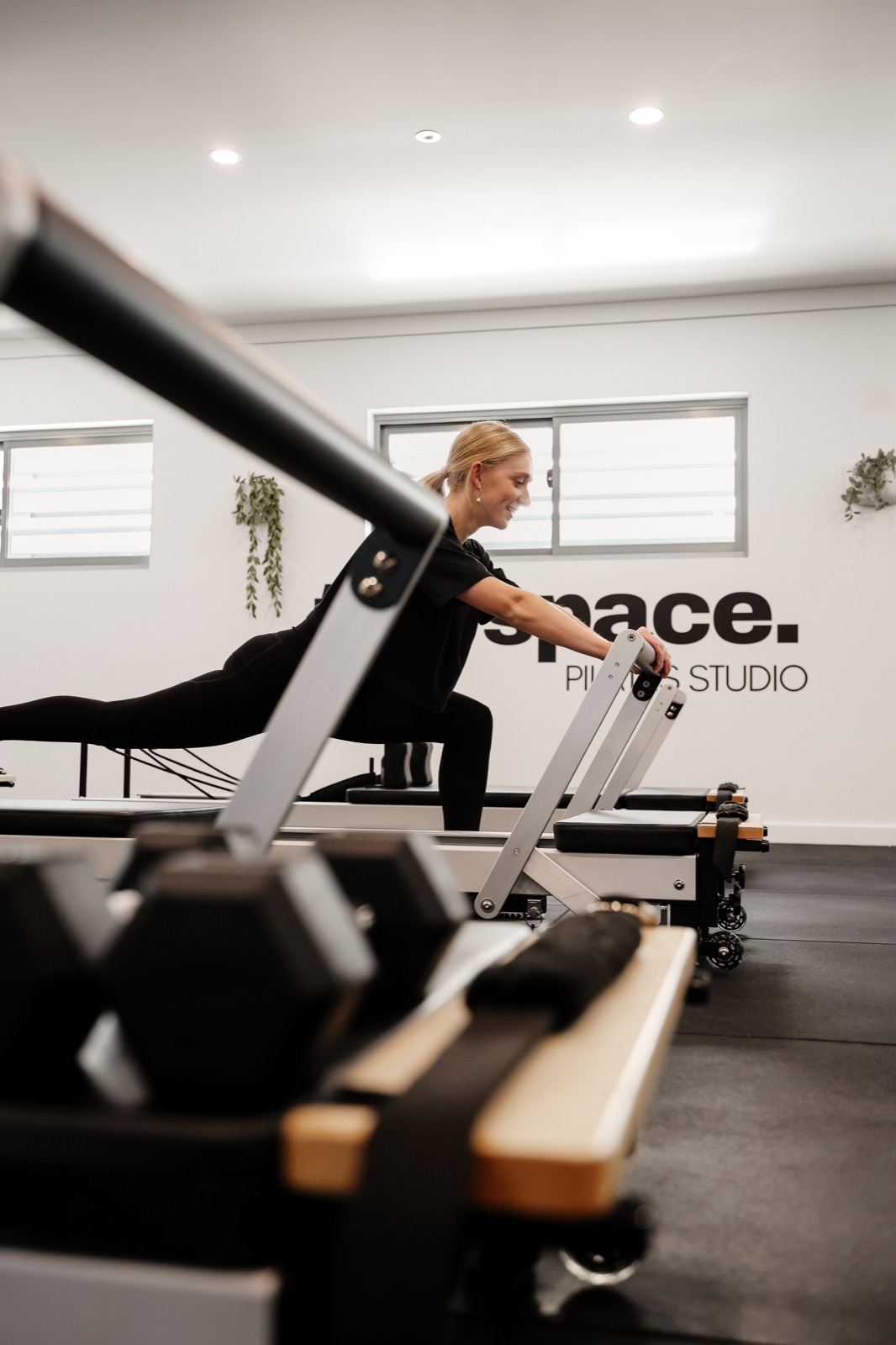 An instructor lunging on a reformer, seen through the studio equipment